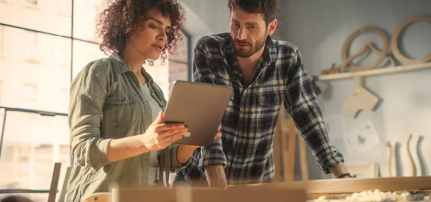 Zwei Handwerker in der Werkstatt bei der Planung nachhaltiger Möbel mit einem Tablet, Symbol für moderne Fertigung, Qualität und verantwortungsbewusste Produktion.